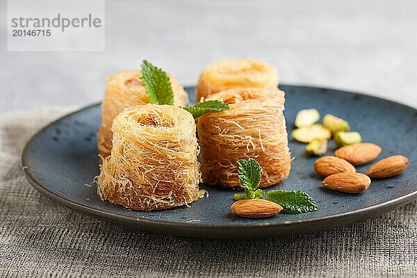 Kunafa  traditionelle arabische Süßigkeiten in blauem Keramikteller auf grauem Betonhintergrund. Seitenansicht  Nahaufnahme  selektiver Fokus