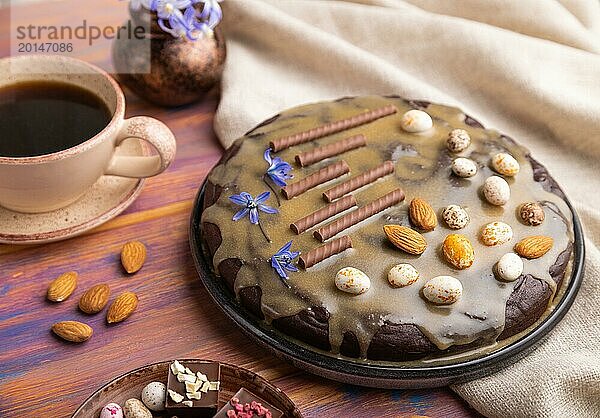 Hausgemachter Schokoladen Brownie Kuchen mit Karamellcreme und Mandeln mit einer Tasse Kaffee auf einem farbigen Holzhintergrund und Leinentuch. Seitenansicht  Nahaufnahme  selektiver Fokus