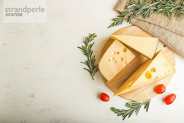 Verschiedene Käsesorten mit Rosmarin und Tomaten auf Holzbrett auf weißem Holzhintergrund und Leinenstoff. Draufsicht  Nahaufnahme  Kopiervorlage  Flat Lay