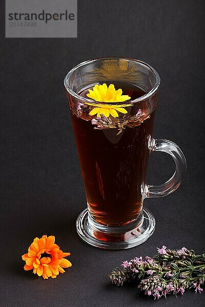 Glas Kräutertee mit Ringelblume und Ysop auf einem schwarzen Hintergrund. Morninig  Frühling  gesundes Getränk Konzept. Seitenansicht  selektiver Fokus  Nahaufnahme