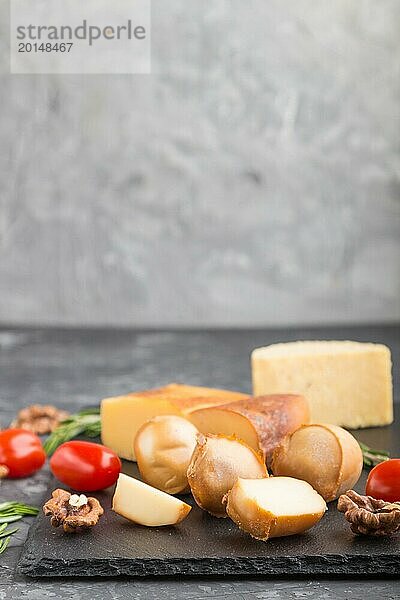 Geräucherter Käse und verschiedene Käsesorten mit Rosmarin und Tomaten auf einer schwarzen Schiefertafel auf einem schwarzen Betonhintergrund. Seitenansicht  Kopierraum  selektiver Fokus