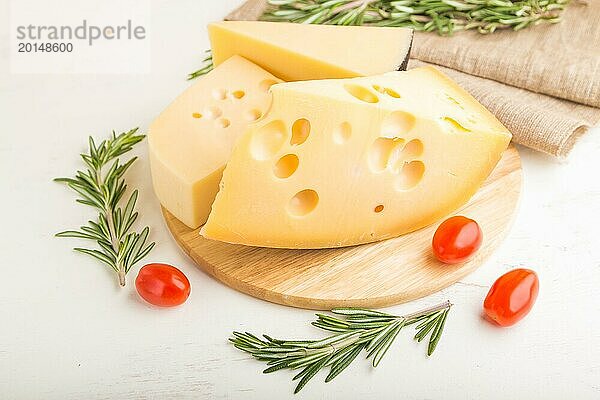 Verschiedene Käsesorten mit Rosmarin und Tomaten auf einem Holzbrett auf einem weißen Holzhintergrund und Leinenstoff. Seitenansicht  Nahaufnahme  selektiver Fokus