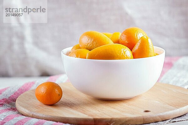 Kumquats in einem weißen Teller auf einem hölzernen Küchenbrett  Nahaufnahme