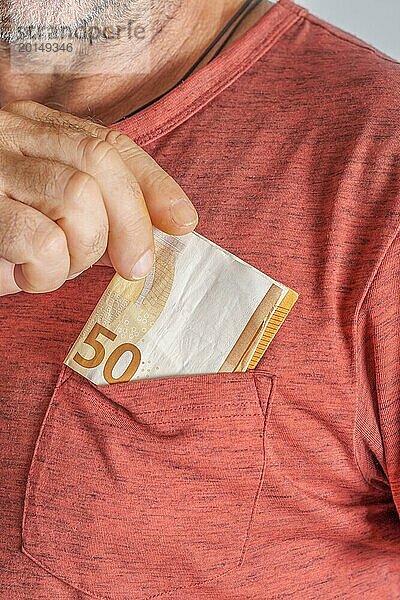 Nahaufnahme eines Mannes  der Euro Banknoten in die Tasche seines roten T Shirts steckt