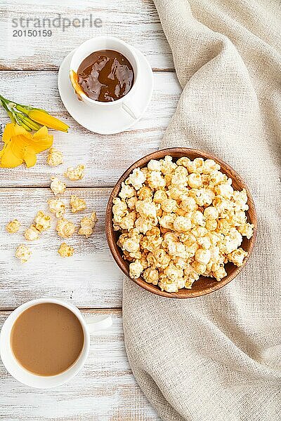 Popcorn mit Karamell in einer Holzschale und einer Tasse Kaffee auf einem weißen Holzhintergrund und Leinenstoff. Draufsicht  flach gelegt  Nahaufnahme