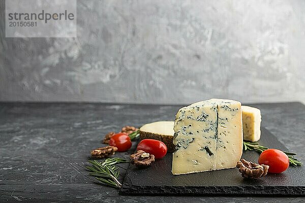 Blauschimmelkäse und verschiedene Käsesorten mit Rosmarin und Tomaten auf einer schwarzen Schiefertafel auf einem schwarzen Betonhintergrund. Seitenansicht  Kopierraum  selektiver Fokus