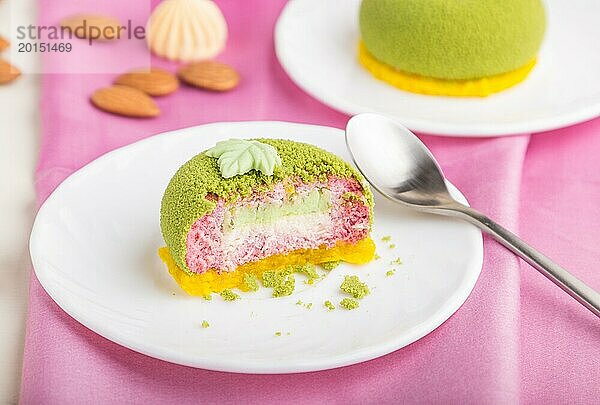 Grüner Mousse Kuchen mit Pistazien und Erdbeersahne auf weißem Holzhintergrund und rosa Stoff. Seitenansicht  Nahaufnahme  selektiver Fokus