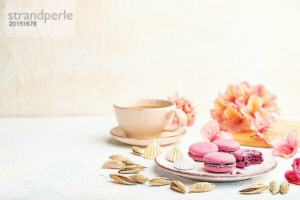 Lila Macarons oder Makronen Kuchen mit Tasse Kaffee auf einem weißen Beton Hintergrund mit Blumen verziert. Seitenansicht  Kopierraum  selektiver Fokus