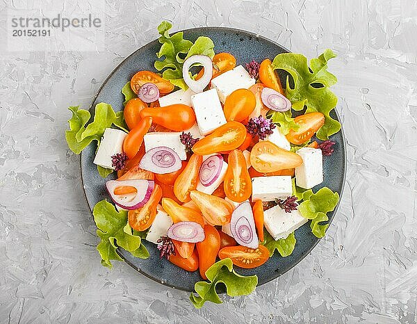 Vegetarischer Salat mit frischen Traubentomaten  Fetakäse  Kopfsalat und Zwiebeln auf blauem Keramikteller auf grauem Betonhintergrund  Draufsicht  Nahaufnahme  flach gelegt