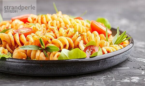 Fusilli Nudeln mit Tomatensauce  Kirschtomaten  Salat und Kräutern auf einem schwarzen Betonhintergrund. Seitenansicht  Nahaufnahme