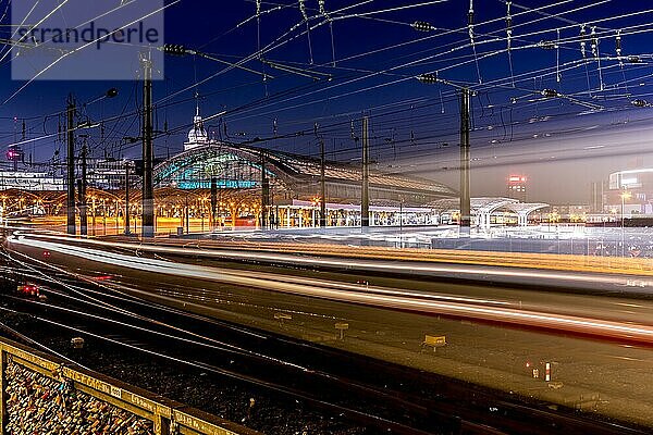 Ein beleuchteter Bahnhof bei Nacht mit Lichtspuren von Zügen  die durch Langzeitbelichtung entstanden sind  Köln Hauptbahnhof bei Nacht