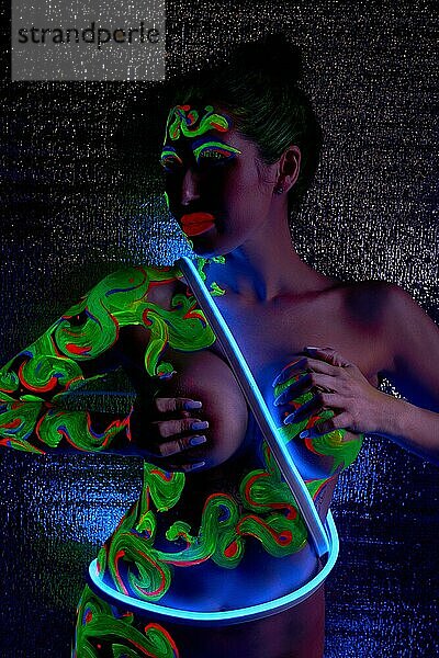 Rückenansicht einer anonymen Frau mit dunklen Haaren und Neon Make up  die mit Körperkunst vor schwarzem Hintergrund steht
