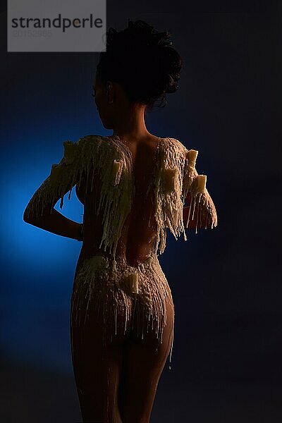 Rückenansicht eines jungen nackten weiblichen Modells mit geschmolzenen Kerzen und Wachs  das den nackten Körper in der Dunkelheit bedeckt