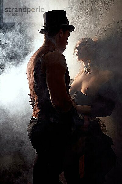 Niedriger Winkel der jungen sexy Frau mit nackter Brust stehen gegen die Wand mit Mann in Steampunk Kostüm durch Rauch umgeben