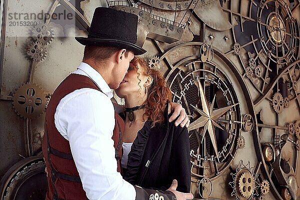 Junge rothaarige Frau und Mann tragen Vintage Steampunk gestylt Outfits stehen in der Nähe von alten Mechanismus und küssen