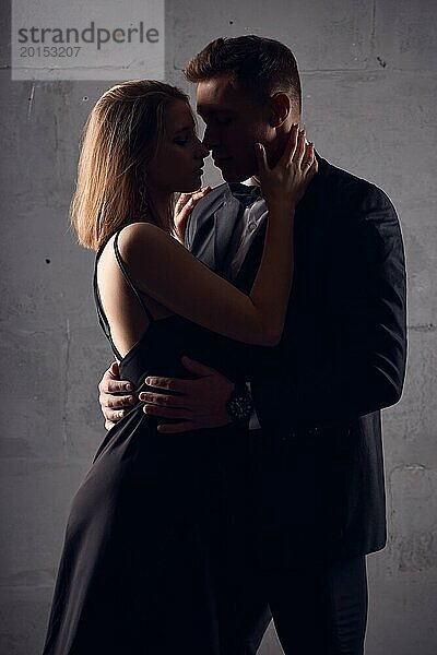 Seitenansicht eines Mannes und einer Frau in schwarzer Abendgarderobe  die sich zum Kuss bereithalten  vor schwarzem Hintergrund