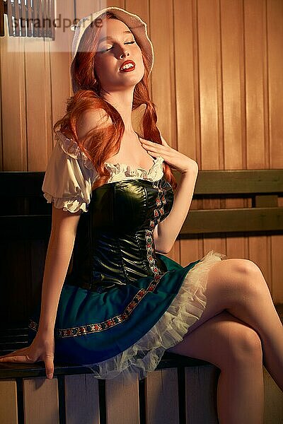 Seitenansicht einer sinnlichen jungen Frau mit zwei Pferdeschwänzen in einem stilvollen deutschen Kleid mit geschlossenen Augen  die auf einer Holzbank sitzt