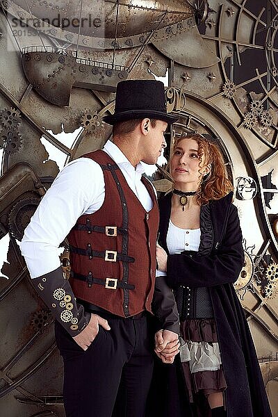 Junge rothaarige Frau und Mann in Vintage Steampunk Kostümen stehen in der Nähe eines alten Mechanismus und schauen sich an