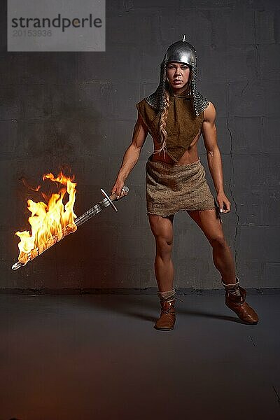 Ganzkörperdarstellung eines selbstbewussten brennenden Ritters in modischem Outfit  der mit einem Lagerfeuer in der Hand steht und in die Kamera schaut  vor schwarzem Hintergrund