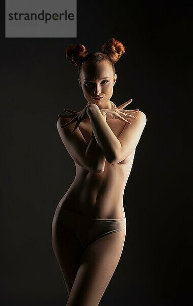 Wunderschöne junge fit verführerische weibliche Modell mit nackten Oberkörper bedeckt Brust mit den Händen und Blick in die Kamera mit Vertrauen gegen schwarzen Hintergrund