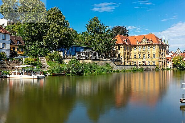 Historisches Gebäude an einem ruhigen Fluss mit Spiegelung im Wasser an einem sonnigen Tag  Villa Concordia mit Fähre in Bamberg