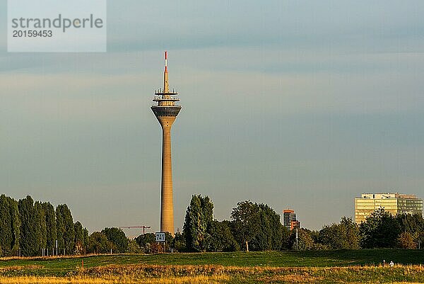 Fernsehturm ragt bei Abenddämmerung mit orangefarbenem Himmel und blauen Wolken über grünem Grasfeld auf  Düsseldorf  Nordrhein- Westfalen