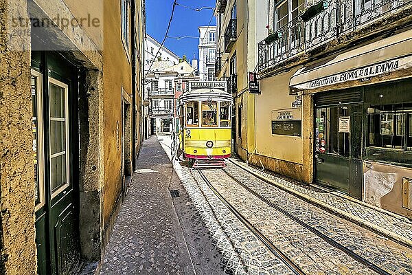 Eine alte gelbe Straßenbahn fährt durch eine enge Gasse mit Kopfsteinpflaster in Lissabon und spiegelt die sonnige  lebhafte Atmosphäre der Stadt wider  Alfama  Lissabon