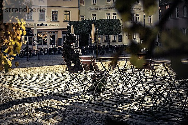 Eine Person sitzt allein an einem Café Tisch  liest entspannt in der herbstlichen Atmosphäre  Auf den Straßen in Weimar