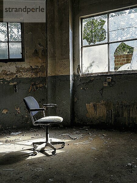 Einzelner Drehstuhl  Bürostuhl in einer leeren verfallenen Fabrikhalle  abblätternde Farbe  Lichteinfall durch kaputte Fensterscheiben  Industrieruine  Innenaufnahme  Lost Place  Deutschland  Europa