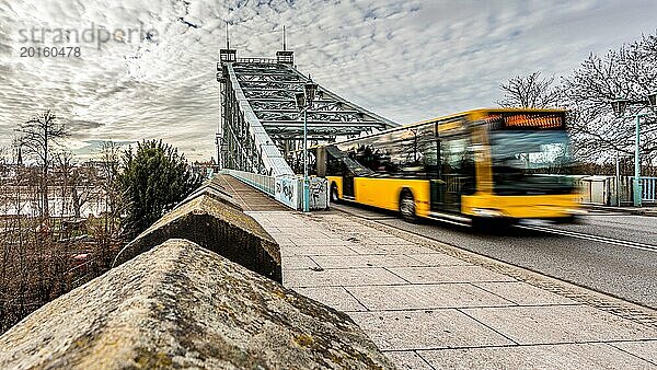 Gelber Bus fährt mit Bewegungsunschärfe an einer Brücke und Mauer vorbei  die Atmosphäre ist dynamisch  Das blaue Wunder in Dresden