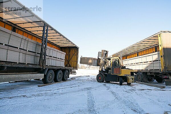 Industriemaschinen mit Lastwagen und Traktor mit schweren Paketen geparkt auf verschneiter Straße im Winter