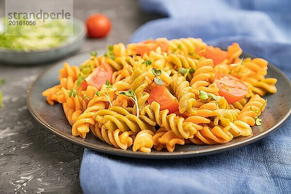 Tortiglioni Grießnudeln mit Tomaten und Mikrogrünsprossen auf einem schwarzen Betonhintergrund und blauem Textil. Seitenansicht  Nahaufnahme  selektiver Fokus