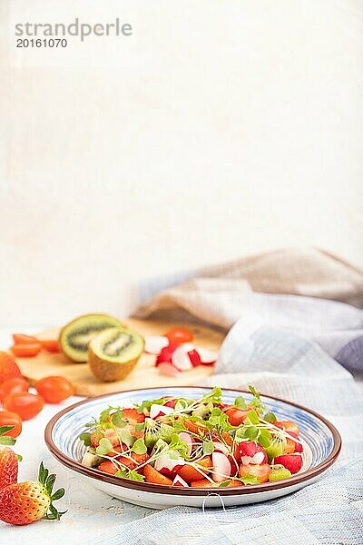 Vegetarischer Obst und Gemüsesalat aus Erdbeeren  Kiwi  Tomaten  Mikrogrünsprossen auf weißem Betonhintergrund und Leinentuch. Seitenansicht  Kopierraum  selektiver Fokus