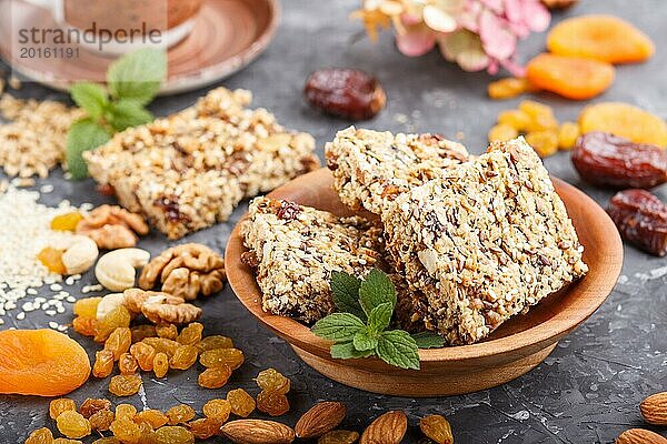 Hausgemachtes Müsli aus Haferflocken  Datteln  getrockneten Aprikosen  Rosinen  Nüssen mit einer Tasse Kaffee auf einem schwarzen Betonhintergrund. Seitenansicht  Nahaufnahme  selektiver Fokus