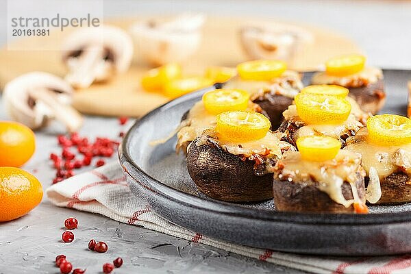 Gefüllte gebratene Champignons mit Käse  Kumquats und grünen Erbsen auf einem grauen Betonhintergrund. Keramikteller  Seitenansicht  Nahaufnahme  selektiver Fokus