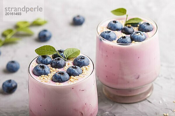 Joghurt mit Blaubeeren und Sesam in einem Glas und Holzlöffel auf grauem Betonhintergrund. Seitenansicht  Nahaufnahme