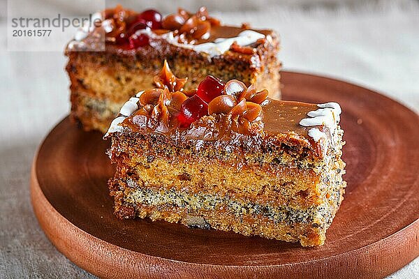 Ein Stück Kuchen mit Karamellcreme und Mohn auf einem hölzernen Küchenbrett. Nahaufnahme  selektiver Fokus  weißer Hintergrund