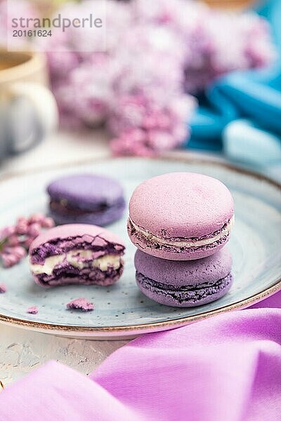 Lila Makronen oder Makronen Kuchen mit Tasse Kaffee auf einem weißen Beton Hintergrund und magenta blauen Textil. Seitenansicht  Nahaufnahme  selektiver Fokus