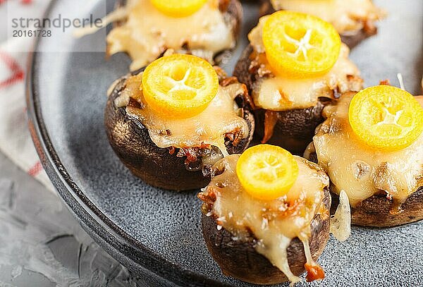 Gefüllte gebratene Champignons mit Käse  Kumquats und grünen Erbsen auf einem grauen Betonhintergrund. Keramikteller  Seitenansicht  Nahaufnahme  selektiver Fokus