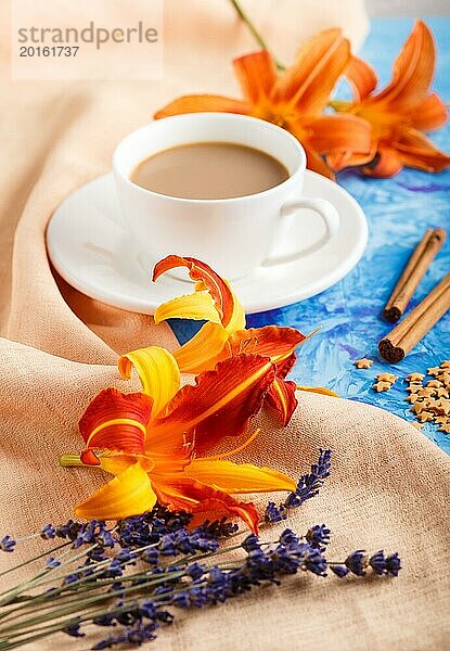 Orange Taglilie und Lavendelblüten und eine Tasse Kaffee auf einem blauen Betonhintergrund  mit orangefarbenem Textil. Morninig  Frühling  Mode Zusammensetzung. Seitenansicht  selektiver Fokus