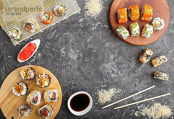 Verschiedene Arten von japanischen Maki Sushi Rollen mit Lachs  Sesam  Käse  Rogen und Essstäbchen  Sojasauce  mariniertem Ingwer auf schwarzem Betonhintergrund. Draufsicht  flat lay  copy space