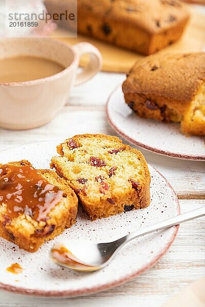 Hausgemachter Kuchen mit Rosinen  Mandeln  weichem Karamell und einer Tasse Kaffee auf einem weißen Holzhintergrund. Seitenansicht  Nahaufnahme  selektiver Fokus