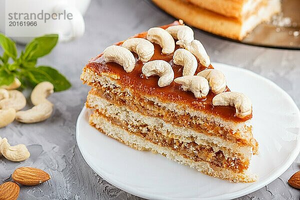 Stück hausgemachter Kuchen mit Karamellcreme und Nüssen mit einer Tasse Kaffee auf einem grauen Betonhintergrund. Seitenansicht  Nahaufnahme  selektiver Fokus