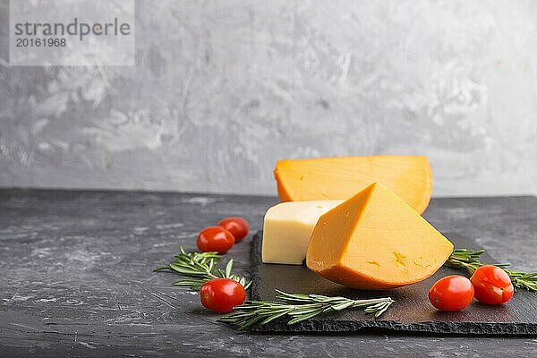 Verschiedene Käsesorten mit Rosmarin und Tomaten auf einer schwarzen Schiefertafel auf einem schwarzen Betonhintergrund. Seitenansicht  Nahaufnahme  Kopierraum  selektiver Fokus