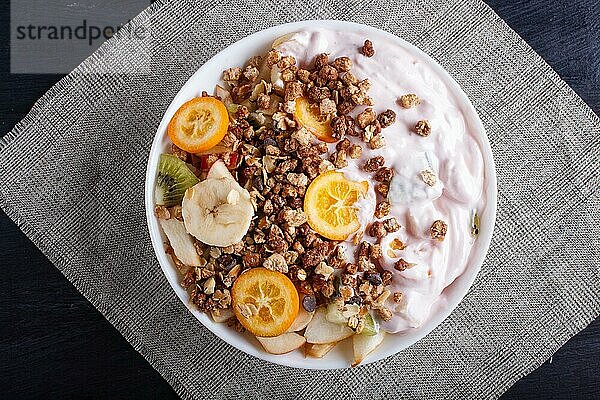 Vegetarischer Salat aus Bananen  Äpfeln  Birnen  Kumquats  Kiwi mit Granola und Joghurt auf schwarzem woodem Hintergrund  Ansicht von oben