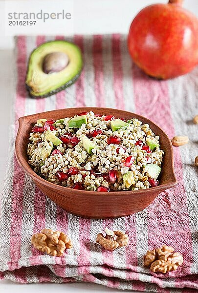 Salat aus gekeimtem Buchweizen  Avocado  Walnuss und Granatapfelkernen in einem Tonteller auf weißem Holzuntergrund. Seitenansicht  Nahaufnahme  selektiver Fokus