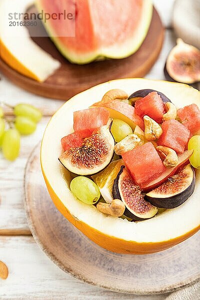 Vegetarischer Obstsalat aus Wassermelone  Trauben  Feigen  Birne  Orange  Cashew auf weißem Holzhintergrund und Leinentuch. Seitenansicht  Nahaufnahme  selektiver Fokus