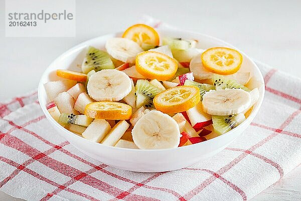 Vegetarischer Salat aus Bananen  Äpfeln  Birnen  Kumquats und Kiwi auf Leinentischdecke  Nahaufnahme  selektiver Fokus. weißer Holzhintergrund