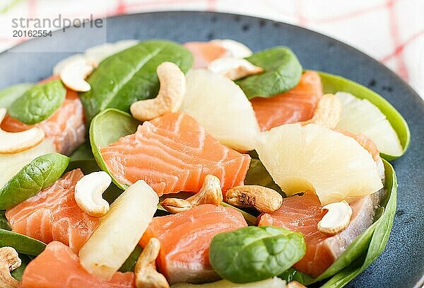 Frischer Lachs mit Ananas  Spinat und Cashew auf einem grauen Betonhintergrund. Seitenansicht  Nahaufnahme  selektiver Fokus  Leinentischdecke