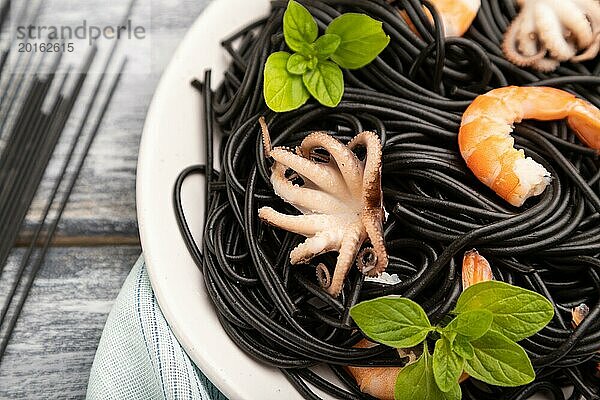 Schwarze Tintenfischnudeln mit Garnelen und kleinen Tintenfischen auf grauem Holzhintergrund und blauem Stoff. Seitenansicht  Nahaufnahme  selektiver Fokus